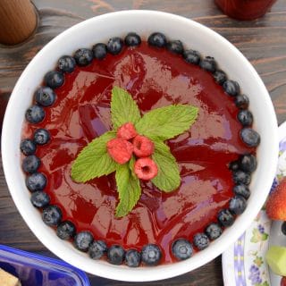 a bowl of red gelatin with fresh blueberries and raspberries